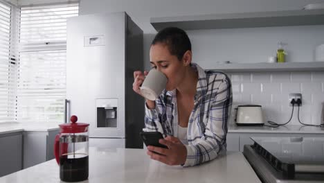 mujer usando un teléfono inteligente y tomando un café en la cocina