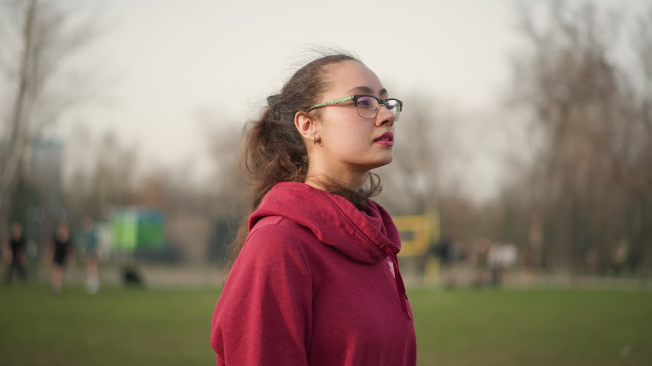 Female Figure Gazing Peacefully Over Landscape, Serene Woman In Red Hoodie Observing Rural View Quietly, Calm Woman With Glasses And Tied Hair Contemplating Tranquil Countryside Backdrop