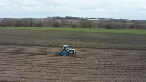 aerial view from side of old blue tractor cultivate crop field, latvia