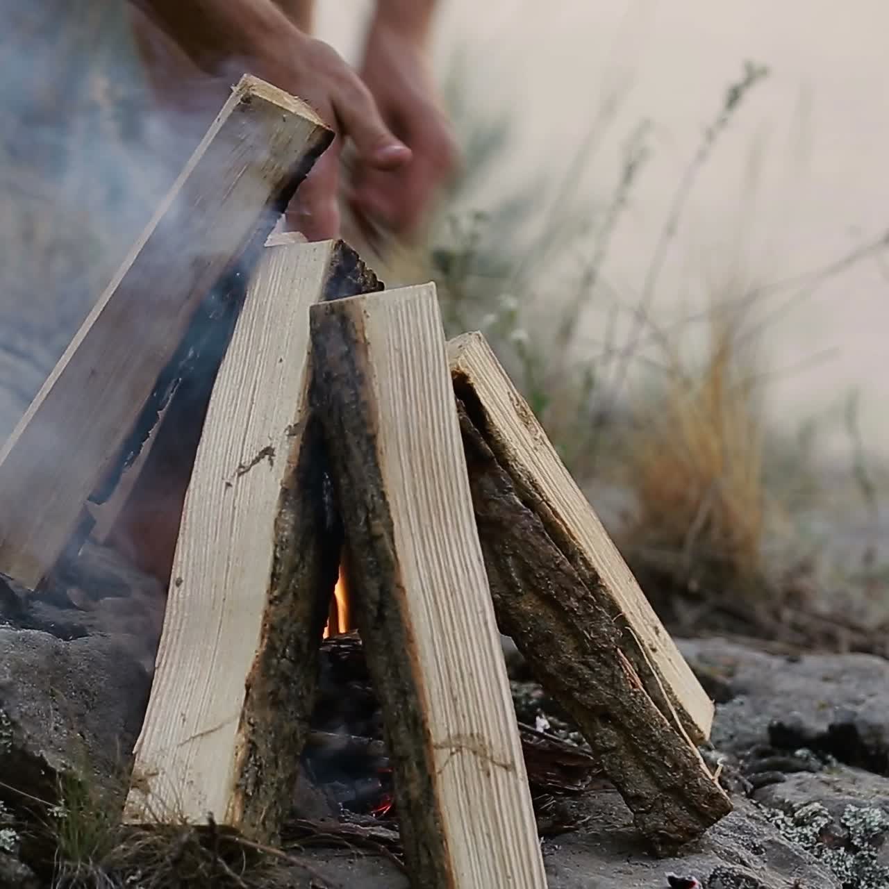 Making Fire In The Forest. Young man kindles a fire in summer wood