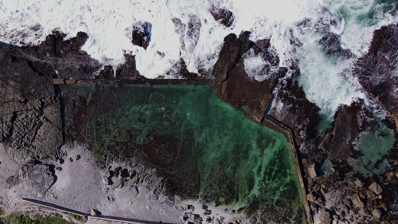 회전하는 무인 항공기가 파도가 부서지는 해안의 조수 웅덩이에서 하강합니다.