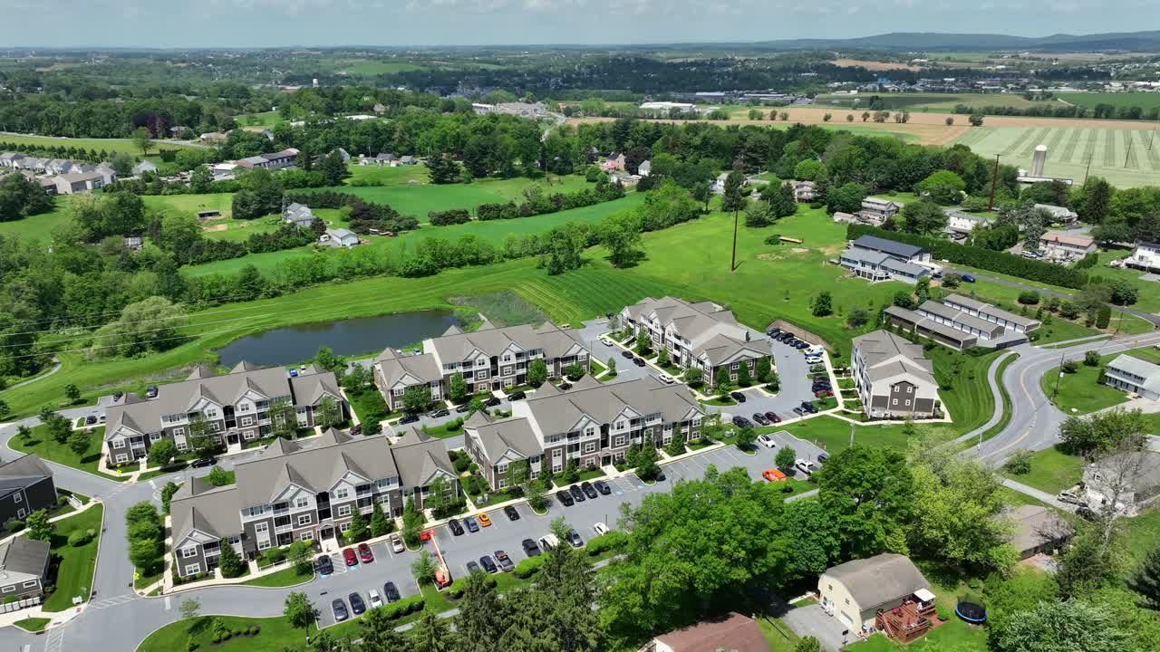 Noble American apartment buildings with pond in green suburb district of town. Sunny day in spring. New building housing architecture in USA. Aerial tilt down shot.
