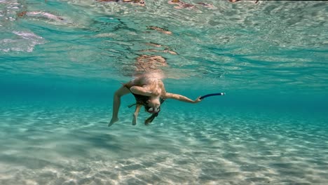 Escena-Submarina-De-Una-Linda-Jovencita-Con-Máscara-De-Buceo-Y-Sosteniendo-Esnórquel-Divirtiéndose-Flotando-En-Agua-De-Mar-Tropical-Pura-Y-Cristalina-De-Una-Isla-Exótica