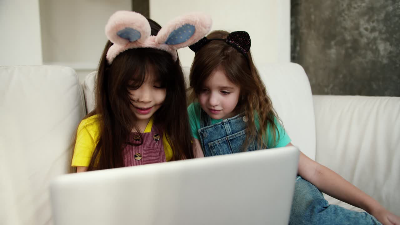 dos hermanas diversas usando una computadora portátil para e-learning o viendo dibujos animados, usando bandas de conejos divertidas