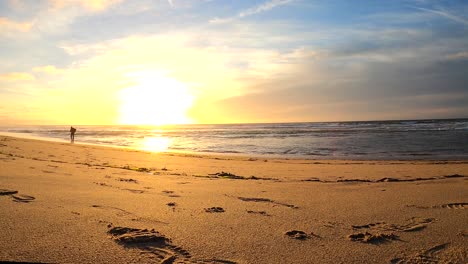 sun setting above the horizon as an isolated man heads back to the sand after beach fishing