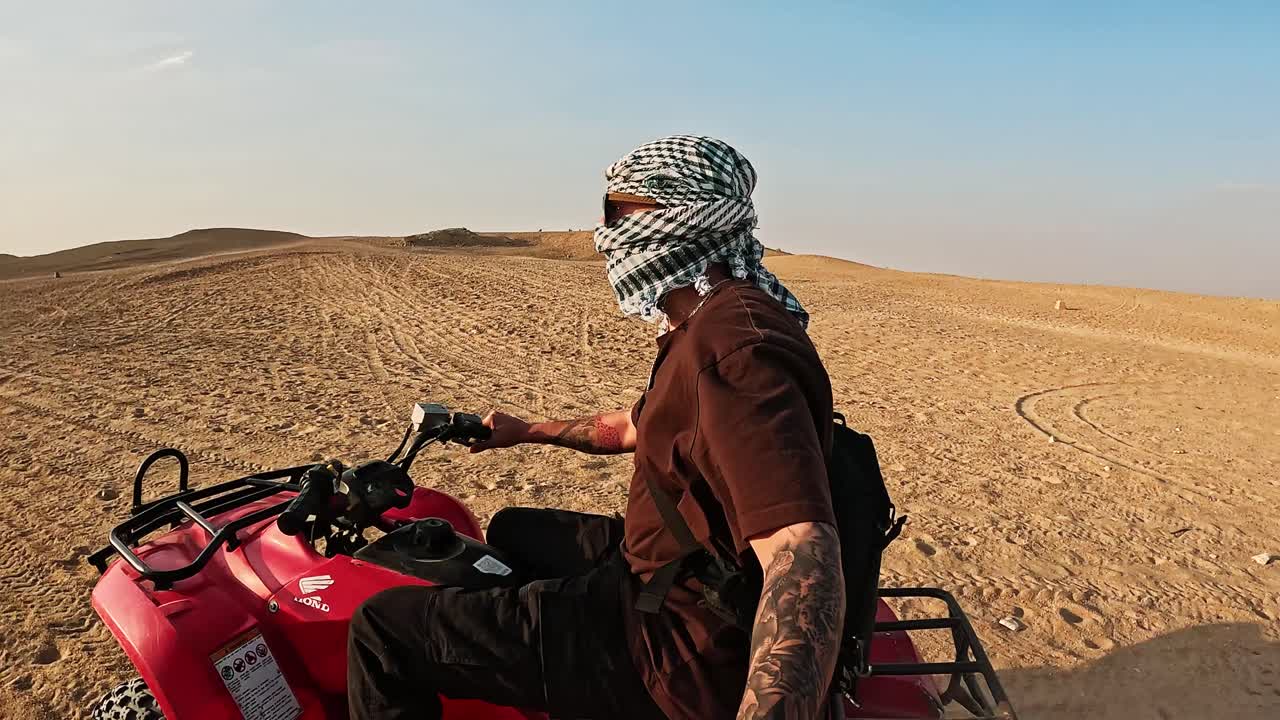 Uomo con kefiah alla guida di un ATV attraverso le dune del deserto.