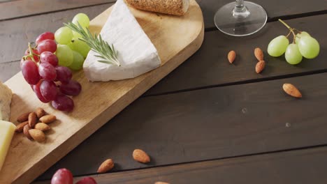 Video-of-cheeses,-bread,-grapes-and-nuts-on-board-and-wine-glass-on-wooden-table,-with-copy-space