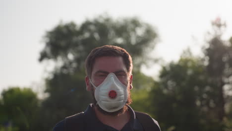 close up of man spraying crops with backpack sprayer wearing mask and glove under golden sunlight creating lens flare while performing outdoor fumigation and pest control on leafy plants