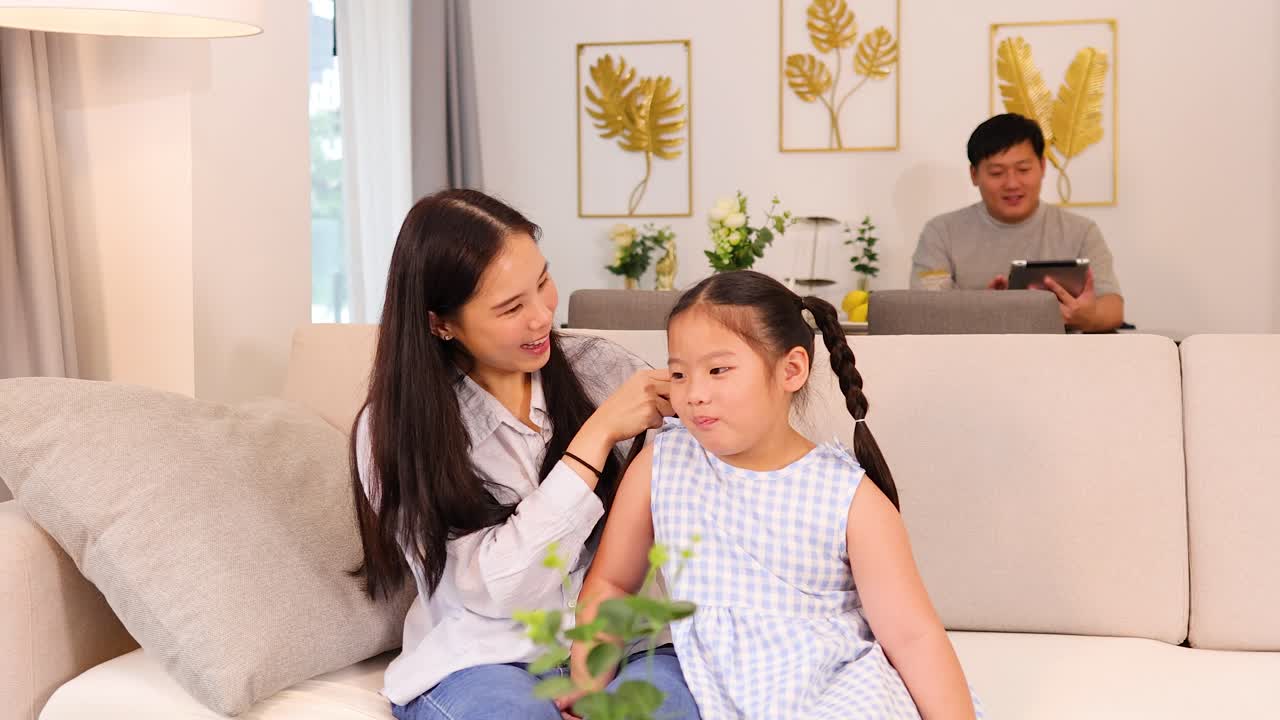 Mother gently consoles sad daughter on sofa, bright natural lighting, cozy modern home interior