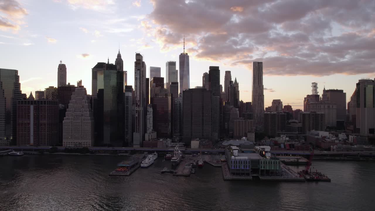 Vista aerea di fronte allo skyline retroilluminato di Lower Manhattan dall'East River, tramonto a New York, USA - ripresa in movimento, ripresa con drone
