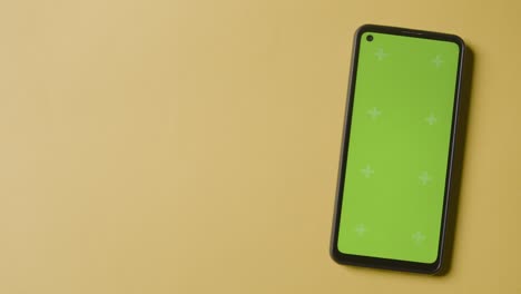 Studio Overhead Shot Of Person Using Green Screen Mobile Phone On Yellow Background