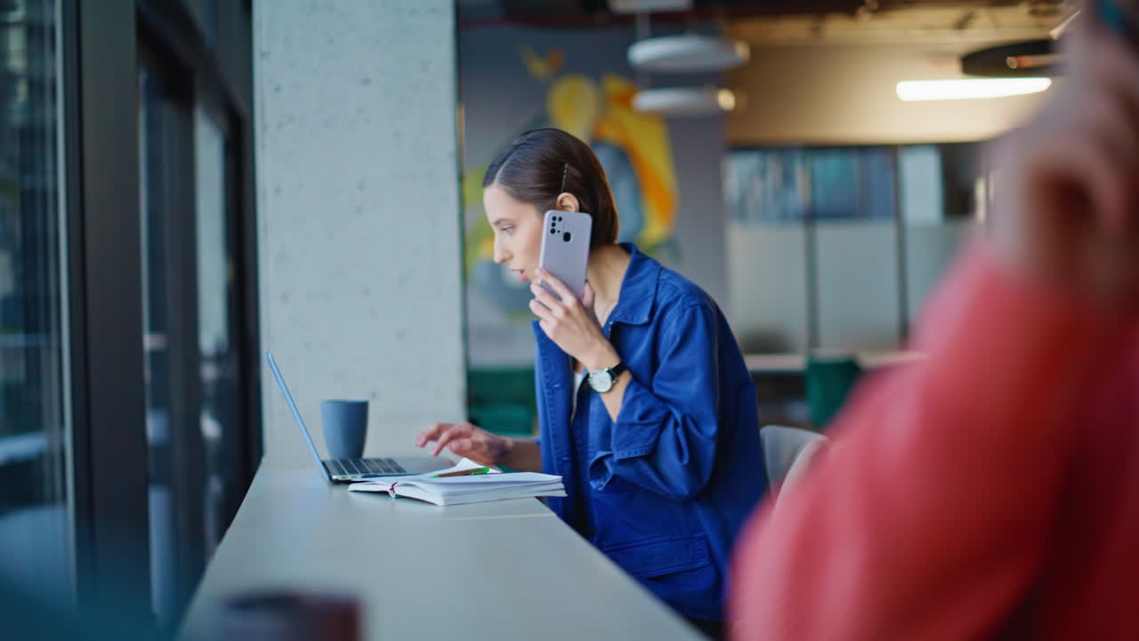 Two freelancers talking mobile phones working at laptops in workspace closeup