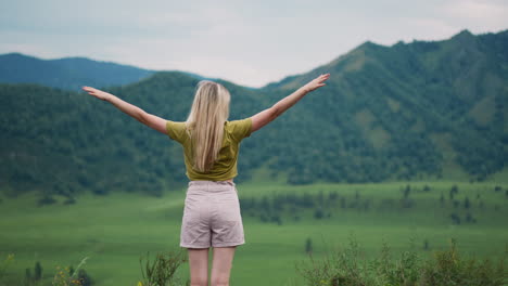 graceful woman hiker with raised hands enjoys green valley