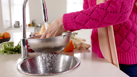 Mid-section-of-biracial-woman-washing-food-in-kitchen-at-home-with-copy-space,-slow-motion