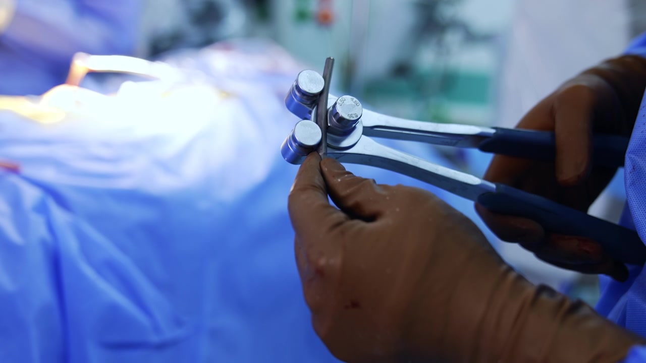 Medicinsk værktøj og materiale i hænderne iført latexhandsker. Læge bruger et instrument til at bøje en metalspån. Nærbillede.