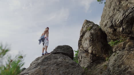 mountain rock climber getting rid of his shirt, bouldering b-roll shot in mountains, rough edge and ridges freeclimbing, sunny bright day, cinematic scenic landscape shot, handsome athletic male