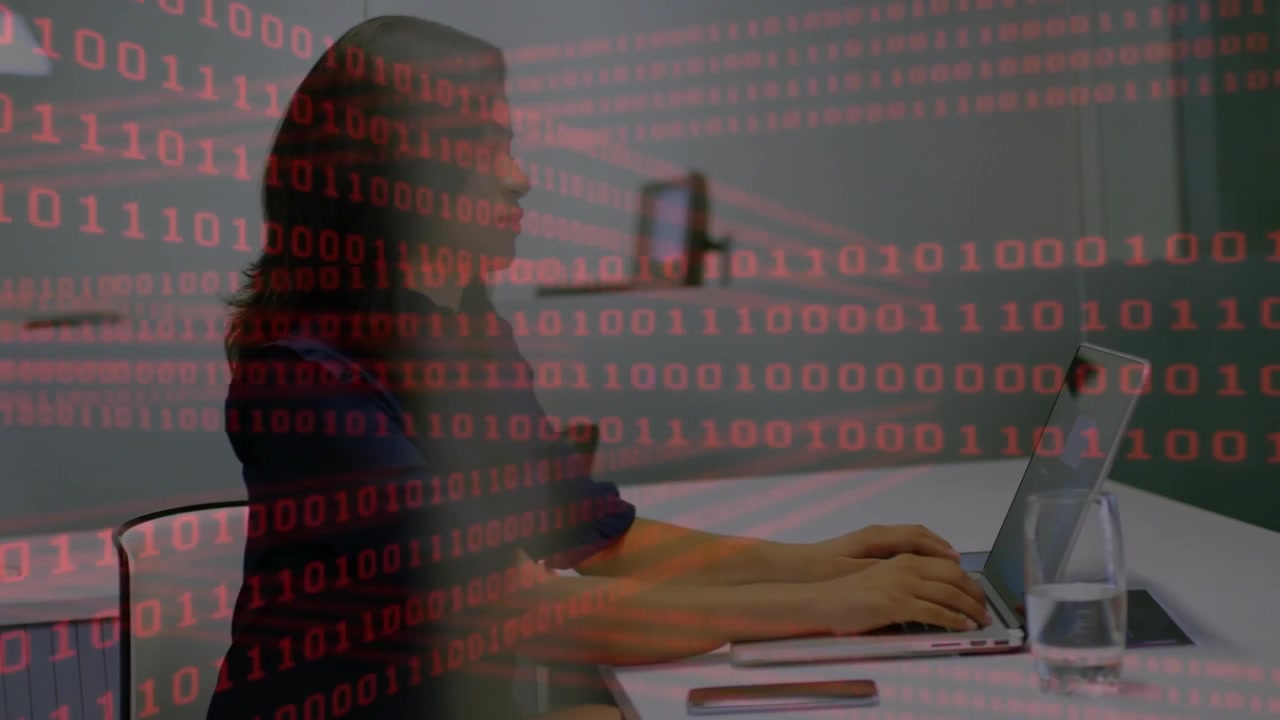 Frau tippt auf Laptop mit Smartphone in der Nähe in einem Technologiebüro, roter Binärcode strömt über den Bildschirm.