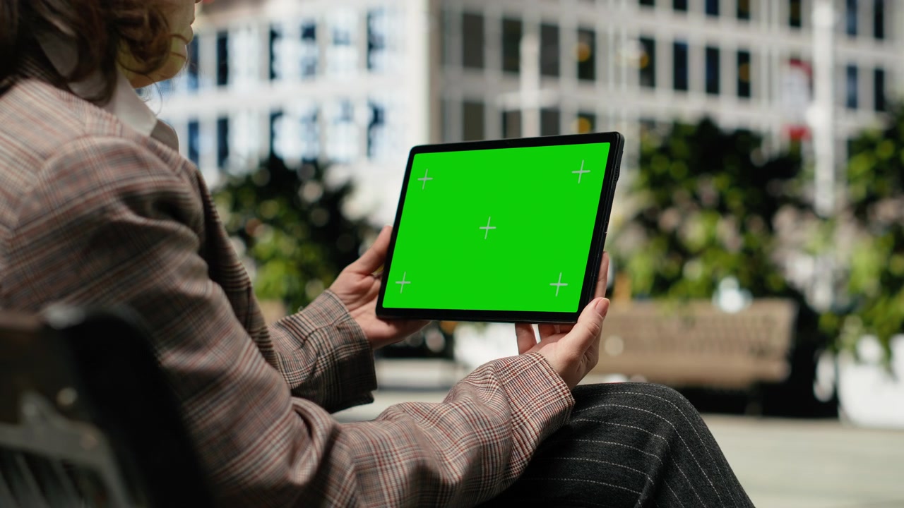 Tablet con schermo isolato usato da una donna mentre si rilassa su una panchina del parco.
