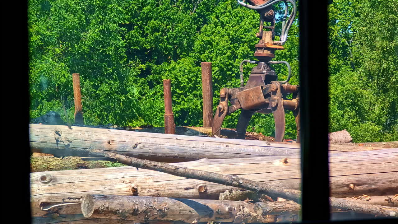Large log truck unloading timber from trailer seen from sawmill window