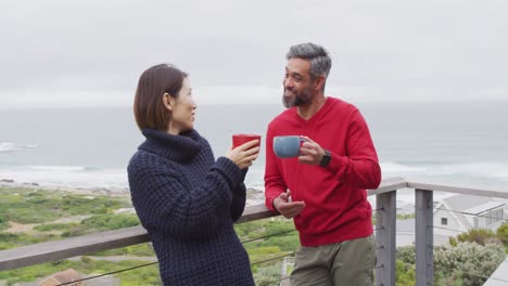 happy diverse couple drinking coffee and talking together on balcony