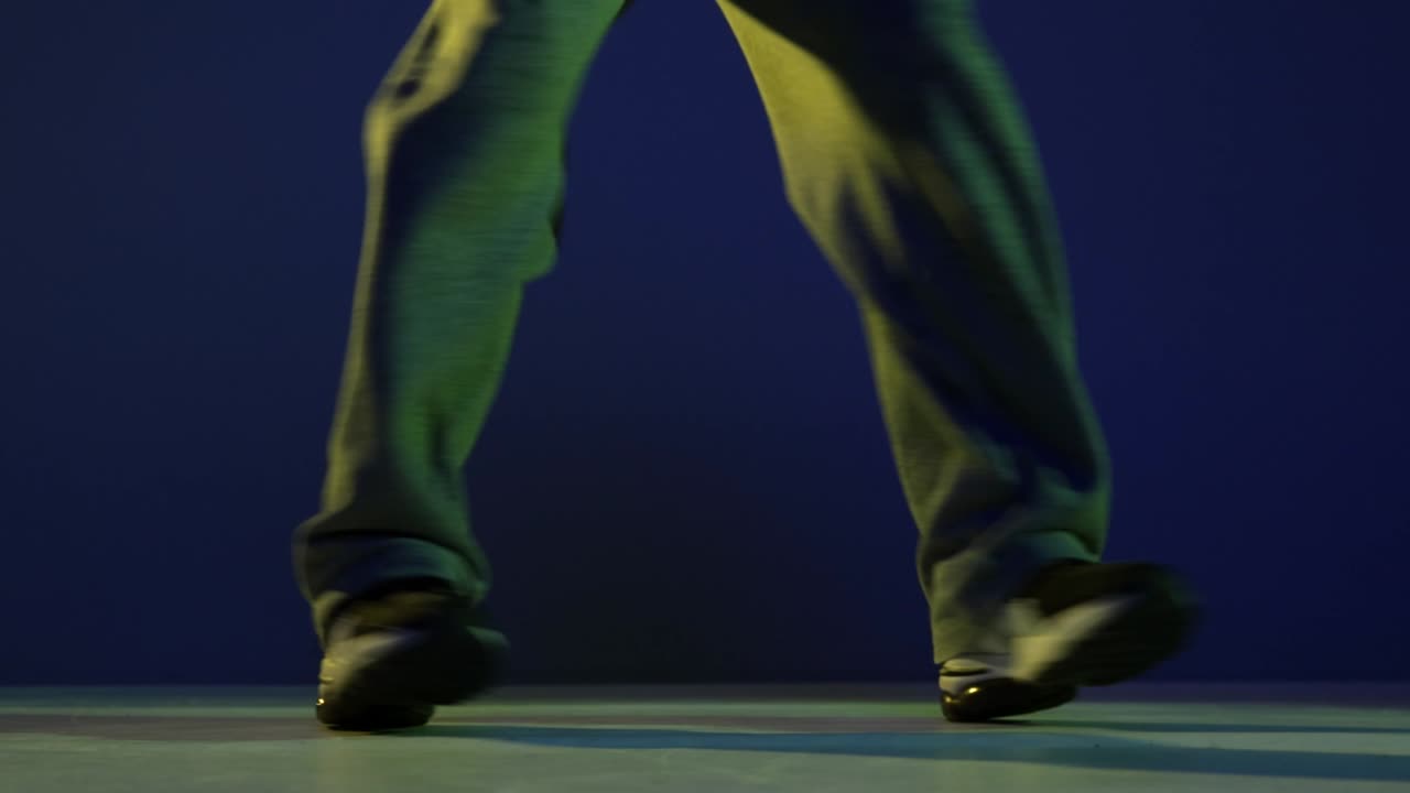 Male legs, hip-hop dancer dancing isolated over dark blue background in neon light. Modern dance art, fashion, youth, ad, style. 4K, video