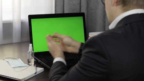 man takes sanitizer bottle and use near laptop with green screen. distance work