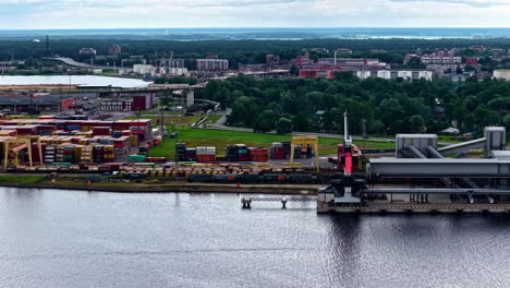 an aerial view shows an intermodal transport hub at the port of riga, where shipping containers are transferred between cargo ships and a freight train on the railway for efficient logistics