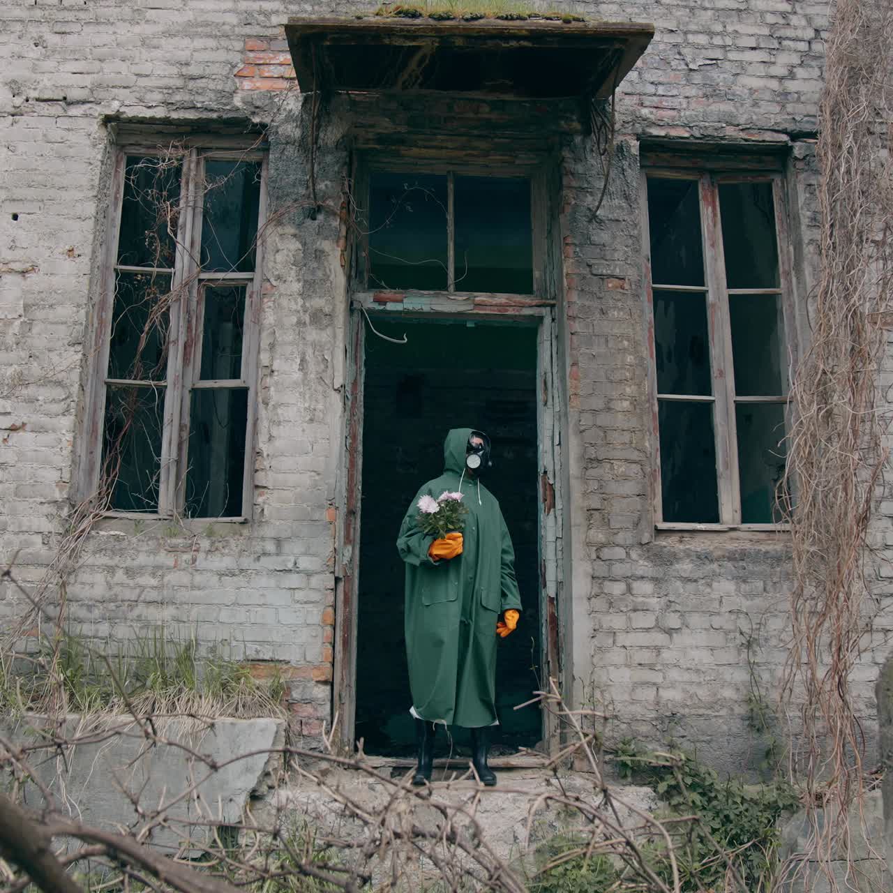 Virologist in radioactive zone. Man in protective suit in broken building. Survivor holding flowers in hands in abandoned place. Chemical attack