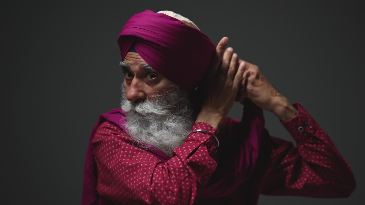 fotografía de iluminación de estudio de baja clave de un anciano sikh con barba atando tela para turbante contra un fondo oscuro tomada en tiempo real 1