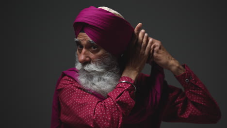 Fotografía-De-Estudio-Con-Iluminación-Tenue-De-Un-Hombre-Sikh-Mayor-Con-Barba-Atando-Una-Tela-Para-Un-Turbante-Contra-Un-Fondo-Oscuro,-Filmada-En-Tiempo-Real-1