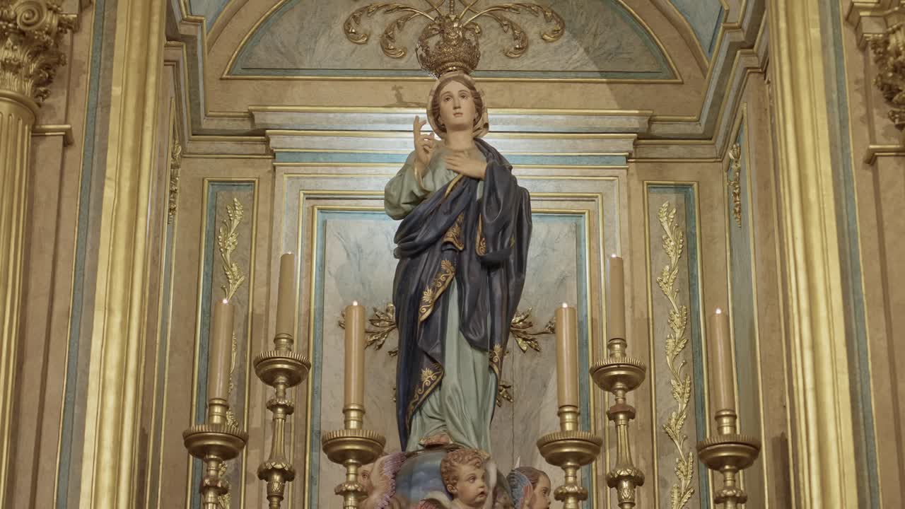 Zdobná socha Panny Marie s korunou obklopená zlatými oltářními svíčkami v kostele