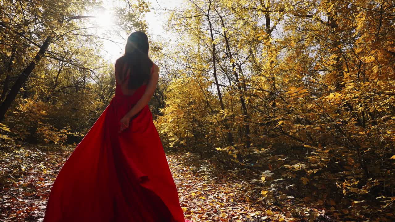 A Woman in a Flowing Red Dress Strolls Through a Golden Forest, Bathed in Ethereal Light; A Beautiful Autumn Scene Capturing Elegance and Nature's Splendor