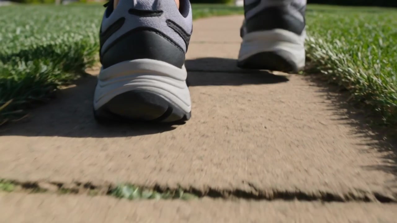 Walking walker wearing athletic shoes and low socks after heel lift along sidewalk casting shadows