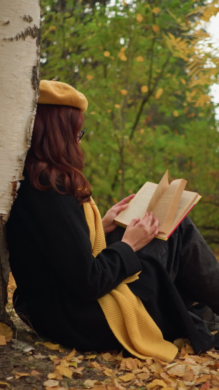 vista lateral de una mujer elegantemente vestida sentada sola, apoyada en un árbol, hojeando páginas de un libro en un entorno pacífico de otoño, rodeada de hojas doradas y una atmósfera de bosque tranquilo