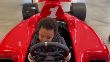 two year old exotic afroeuropean baby enjoying in a f-1 toy red car inside a mall