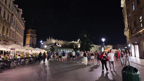 nighttime view of bustling main square, featuring lights, people, and historic architecture