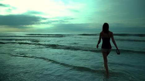 young woman walking in the ocean at sunset