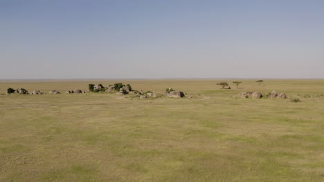 Stone-island-in-Serengeti-valley-with-a-safari-tour-car-parked-in-the-shadow-of-the-tree-in-the-background,-Tanzania