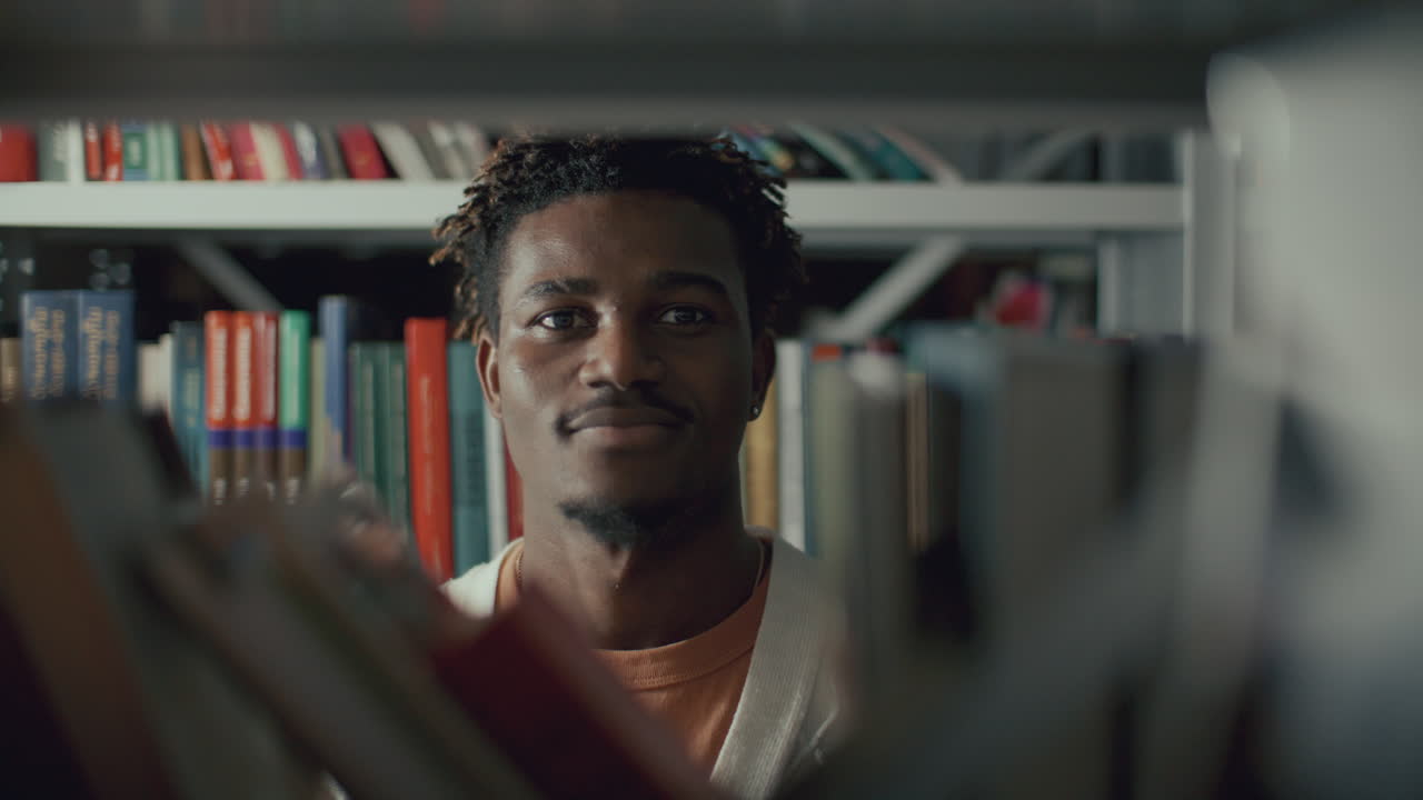 retrato de un joven negro de pie en la biblioteca y sonriendo a la cámara