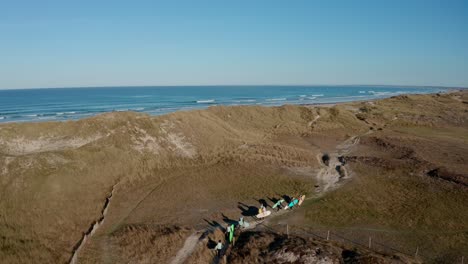 Surfers-carrying-boards-along-a-sandy-trail-in-coastal-dunes,-aerial-view