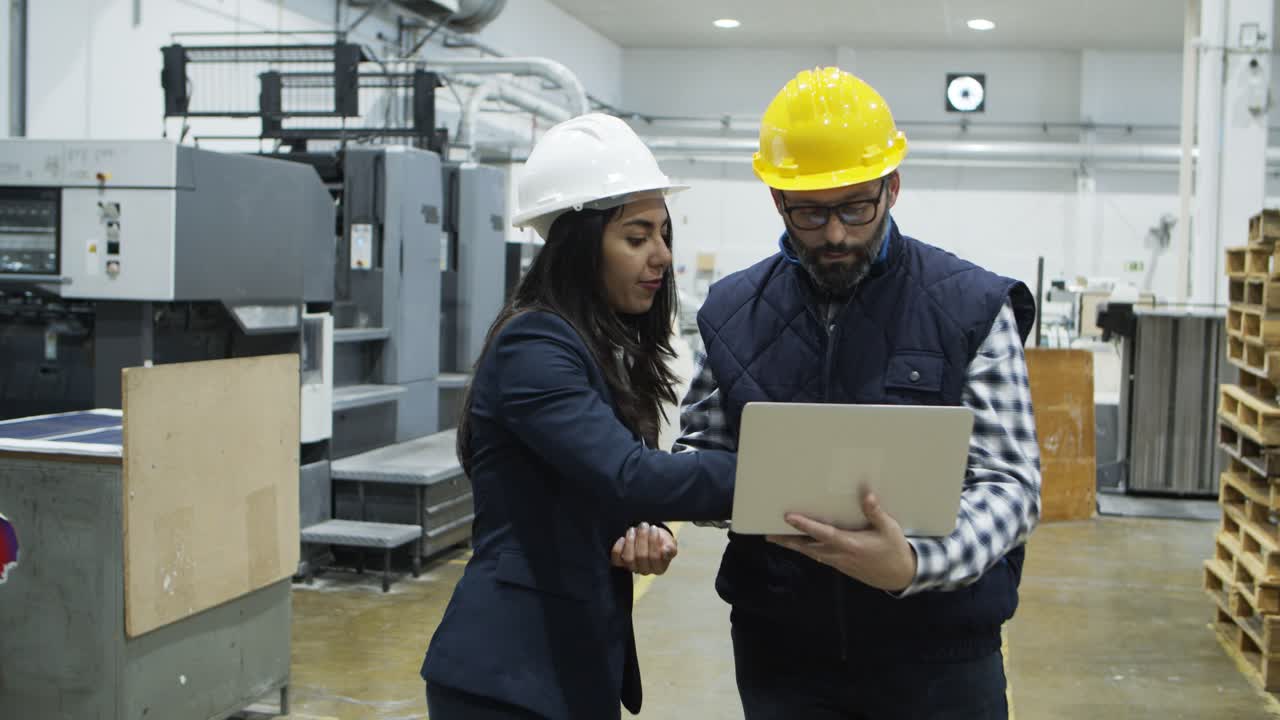 Confident workers standing with laptop at factory and talking