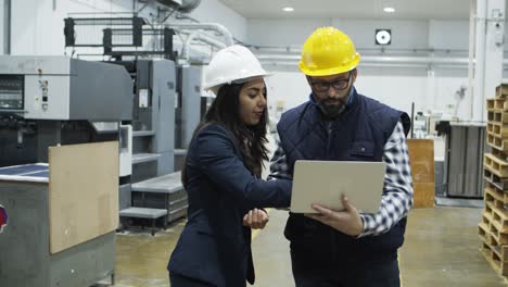 Confident-workers-standing-with-laptop-at-factory-and-talking