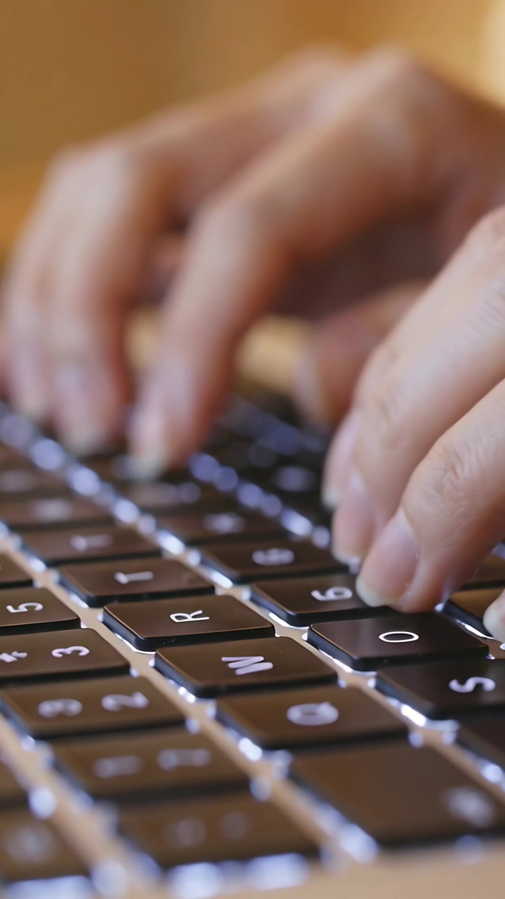 Vertical video: Starting poised fingers, hands typing and pressing keys on backlit keyboard at desk
