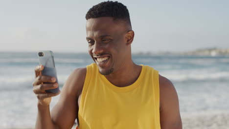 Joven-Afroamericano-En-Forma-Tomando-Fotos-Usando-Un-Teléfono-Inteligente-Sonriendo-Disfrutando-De-La-Tecnología-Móvil-En-Vacaciones-En-La-Playa-Usando-Chaleco-Amarillo