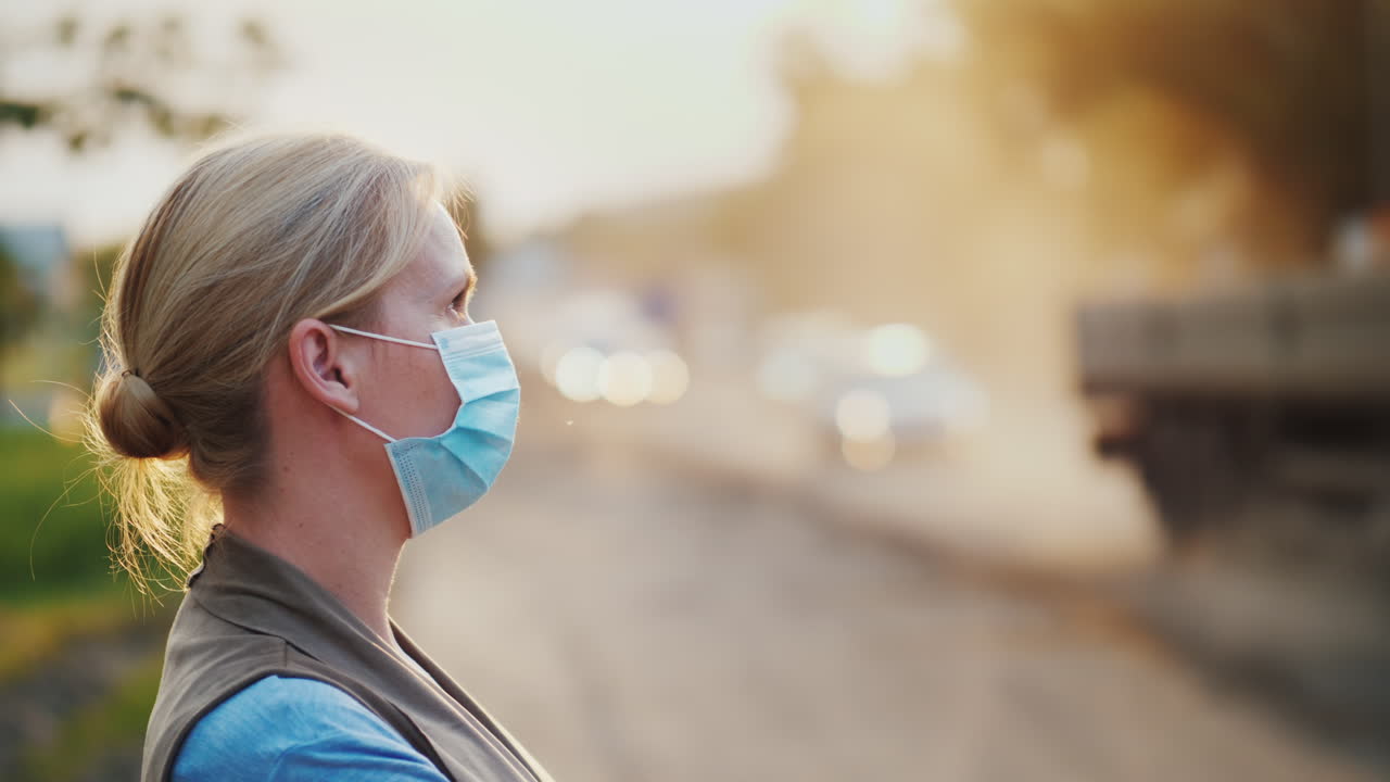 더러운 공기 - 거즈 붕대를 감은 한 여성이 차량 생태 문제가 가득한 도로 근처에 서 있습니다.