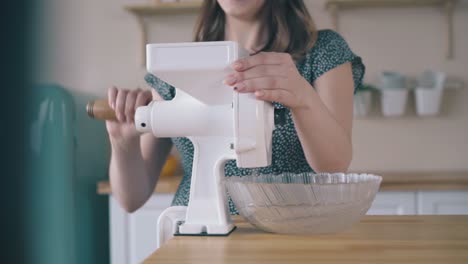 woman-turns-handle-of-domestic-flour-mill-on-kitchen-table