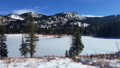 tilt up handheld extreme wide landscape nature shot of the frozen silver lake surrounded by pine trees in the famous ski town of brighton, utah on a sunny warm winter day