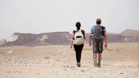 pareja de aventureros caminando por el valle, montañas al fondo, desierto de israel, día nublado, tiro estático