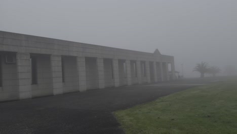 spooky view of a modern stone building covered in fog next to a green field