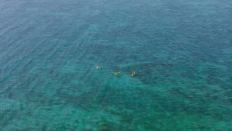 Drei-Personen-In-Gelben-Kajaks-Paddeln-Im-Seichten-Blauen-Tropischen-Wasser,-Aus-Der-Luft